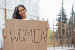 Pretty girl with curly hair stands with handmade feminist poster in hands